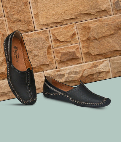 Black Big Boon men's ethnic shoes with laser design and stitched detailing against stone wall background